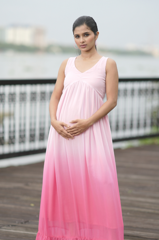 Angled view of Blush Ombre Maternity Evening Gown, featuring a sleeveless design and a soft pink ombre, offering a comfortable and elegant fit.