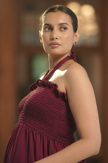  Angled view of Maroon Halter-Neck Maternity Evening Gown, featuring a smocked bodice and flowing skirt, perfect for moms-to-be attending formal events.